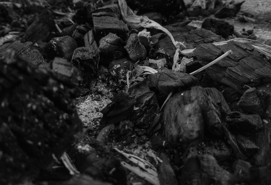 An artistic black and white close-up of charcoal and wood remnants after a fire.