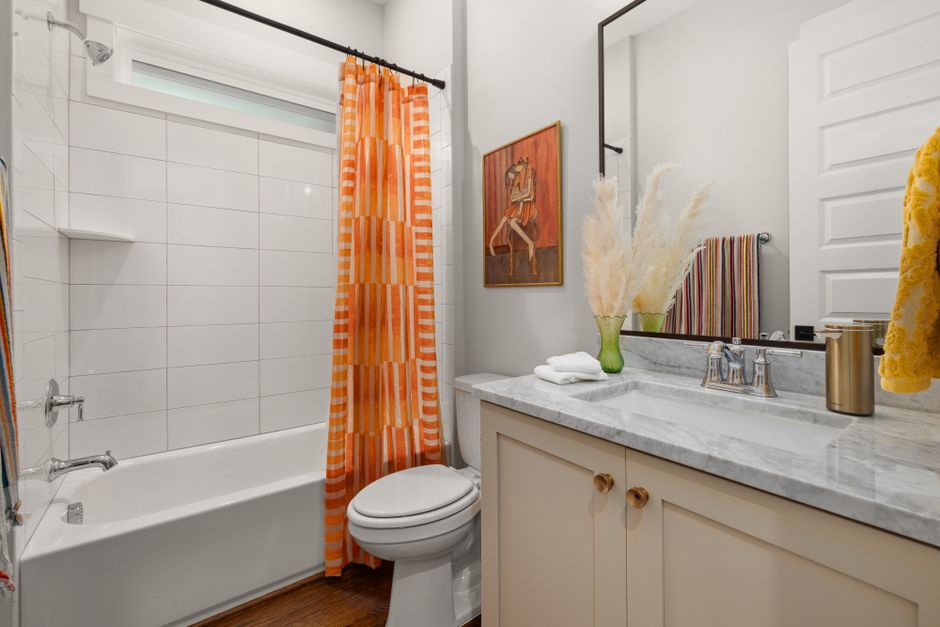 Bright bathroom featuring an orange-striped shower curtain and a marble countertop for a modern look.